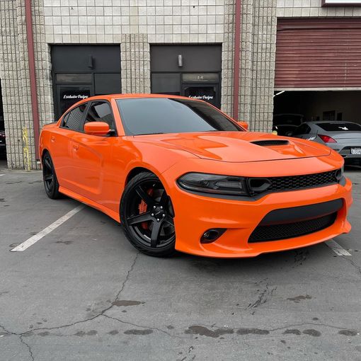An orange dodge charger is parked in a parking lot in front of a building.
