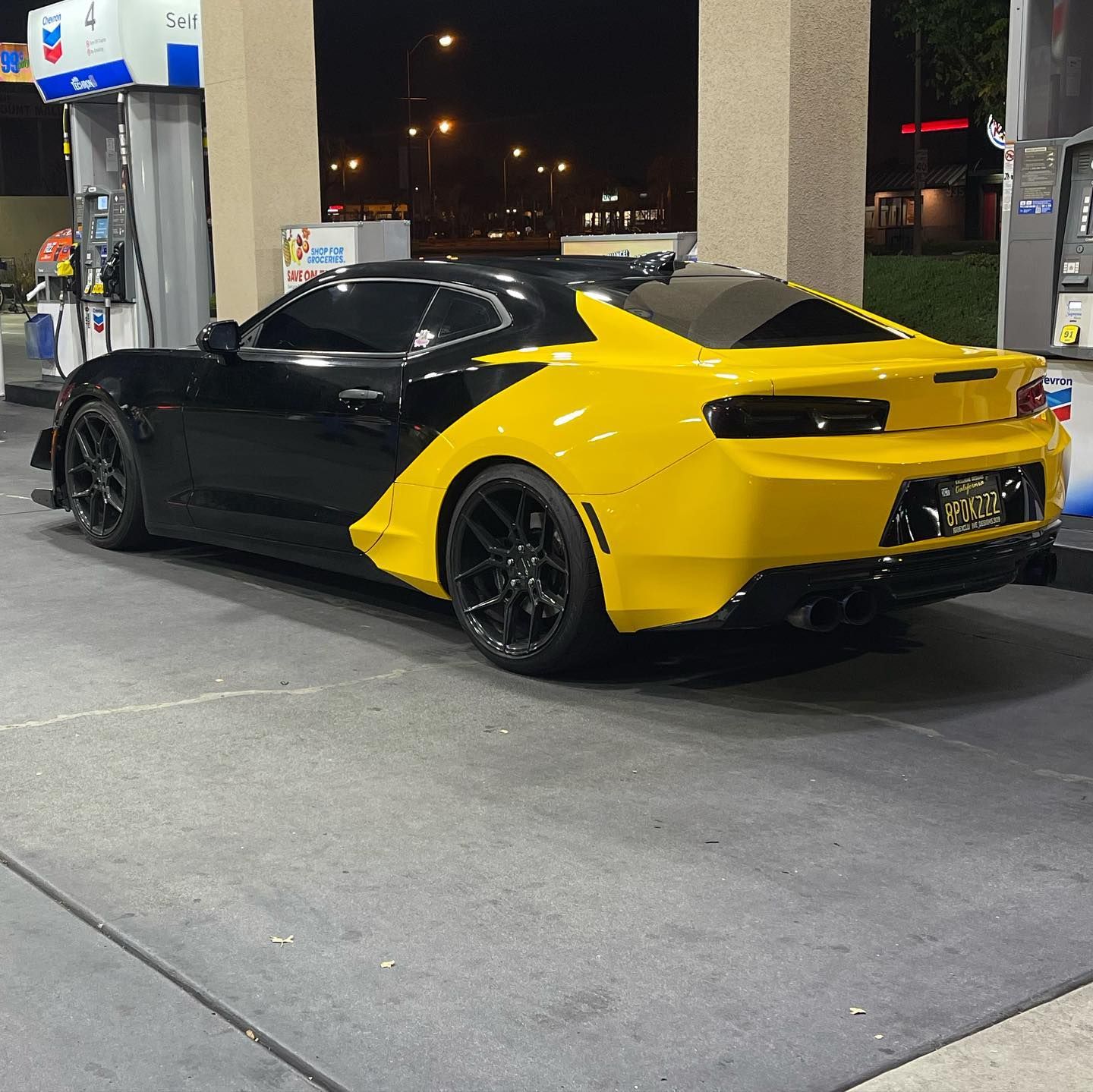 A black and yellow sports car is parked at a gas station