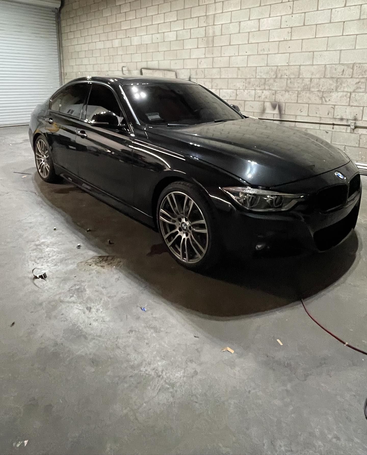 A black car is parked in a garage next to a brick wall.