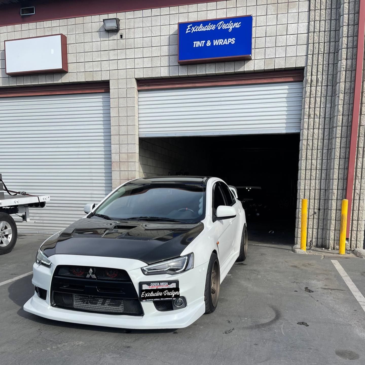 A white car is parked in front of a building that says tint & wraps