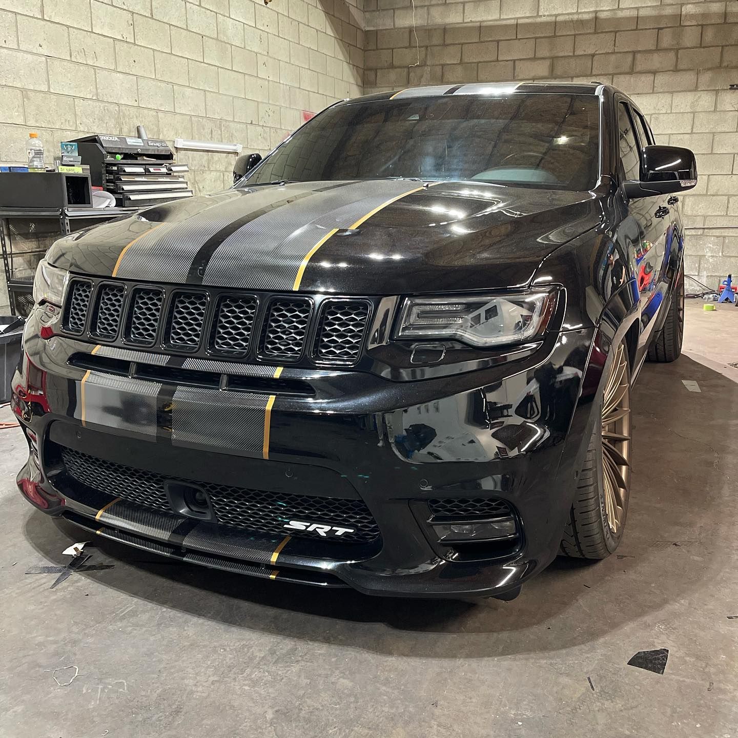A black jeep grand cherokee with a yellow stripe on the hood is parked in a garage.