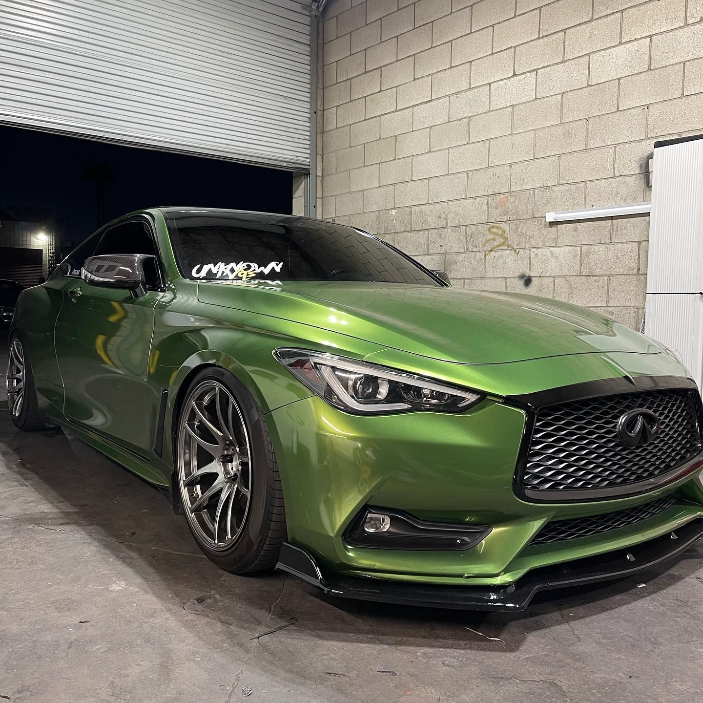 A green car is parked in a garage next to a brick wall.