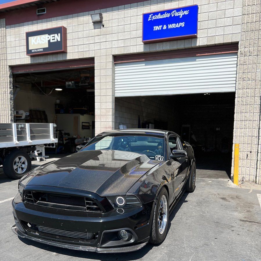 A black mustang is parked in front of a garage