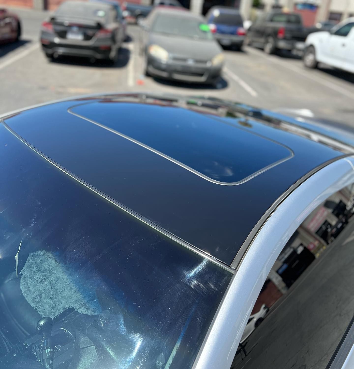A black car with a sunroof is parked in a parking lot
