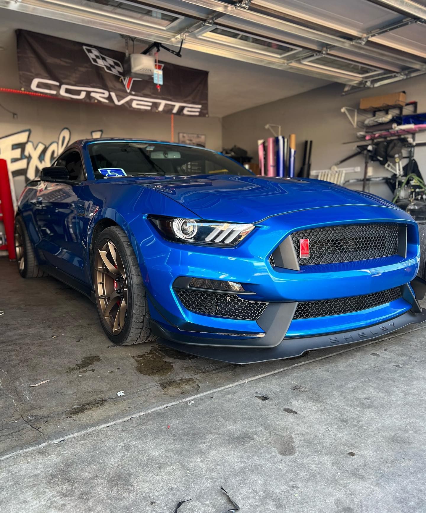 A blue mustang is parked in a garage next to a corvette banner.