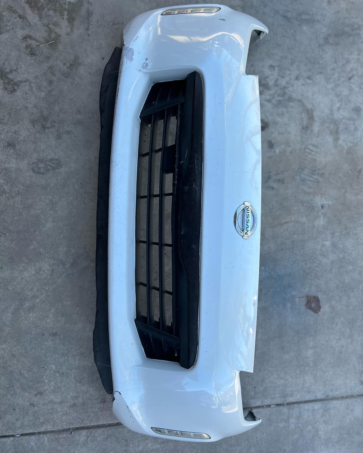 A white nissan bumper is sitting on a concrete surface.