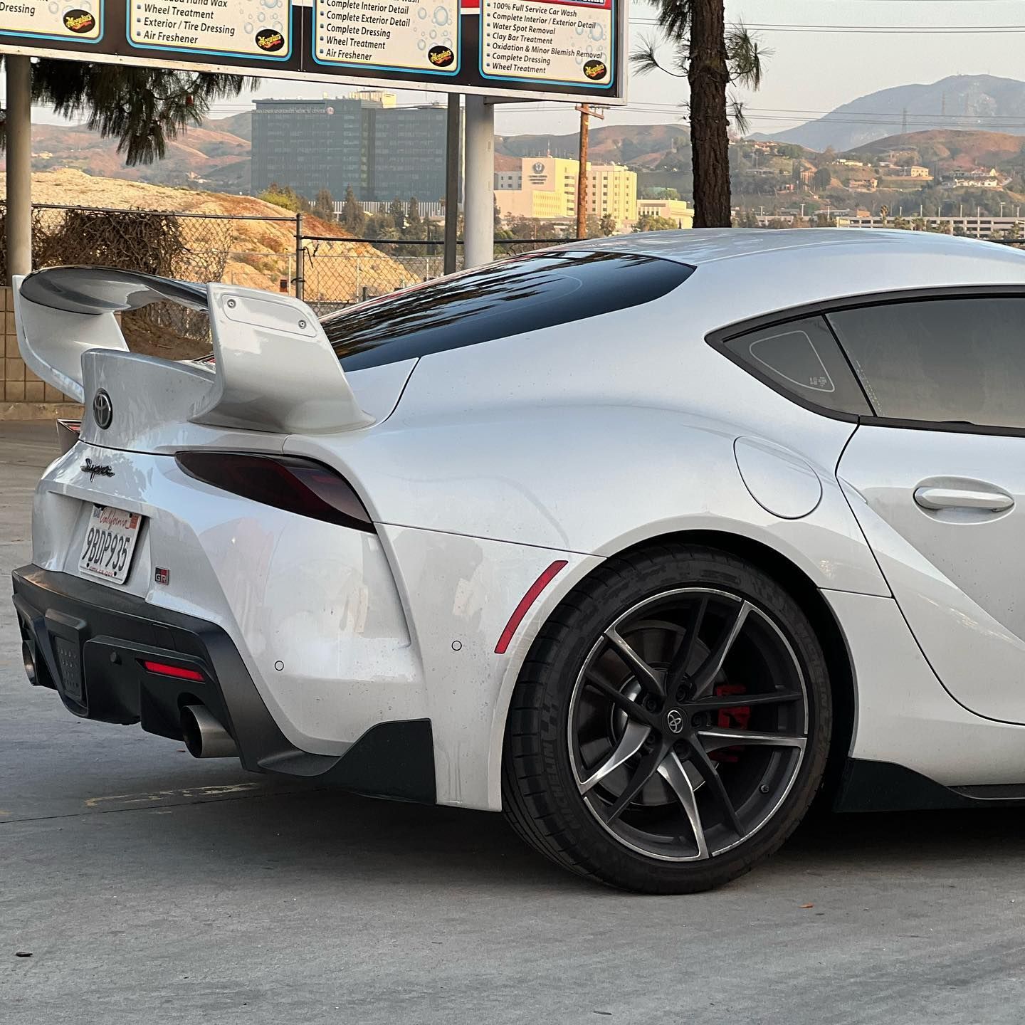 A silver sports car with a wing is parked in a parking lot.