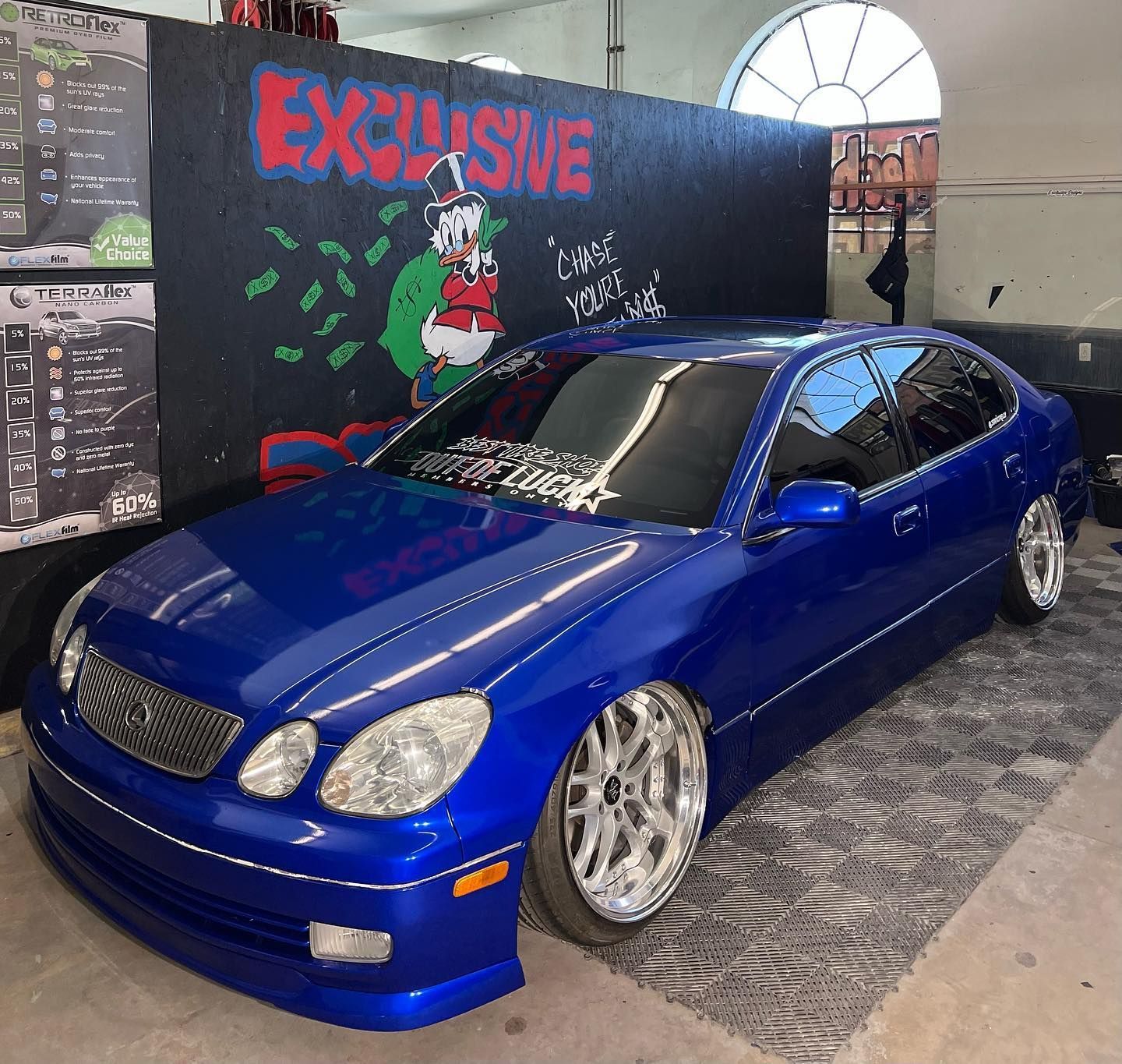 A blue car is parked in front of a wall that says exclusive