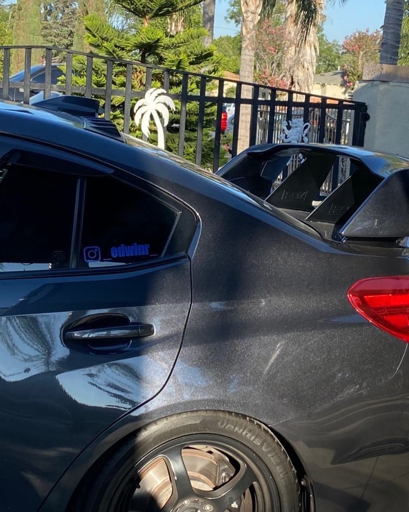 A black car is parked in front of a fence.