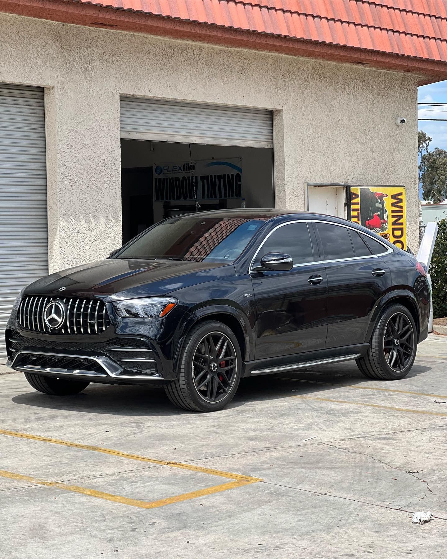 A black car is parked in a parking lot in front of a building.