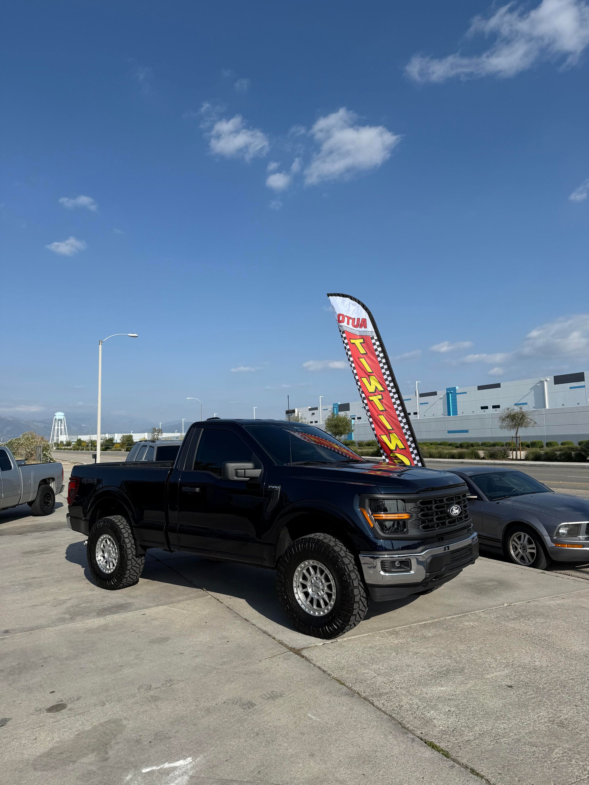 A black truck is parked in a parking lot with a flag on top of it.