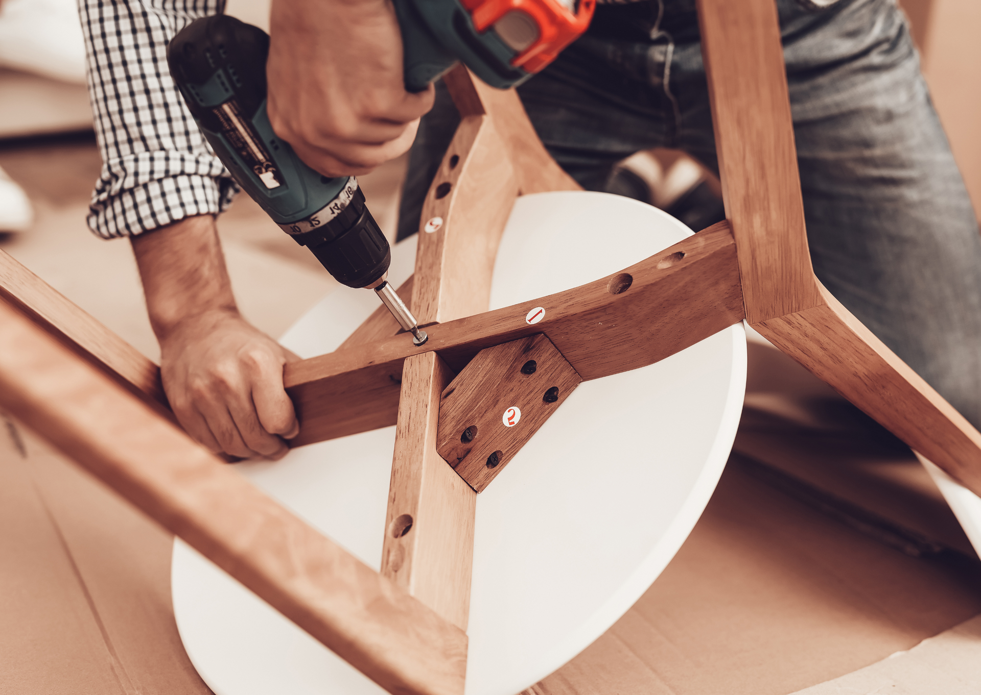 Person assembling a wooden chair with a power drill.