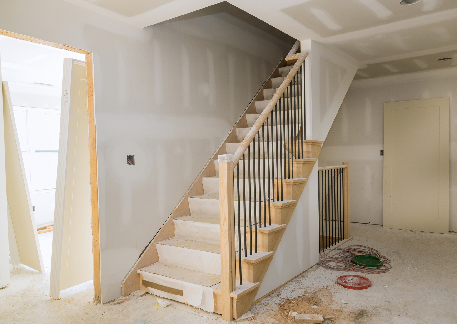 Staircase under construction with wooden steps, black iron railings, and drywall in a new home.