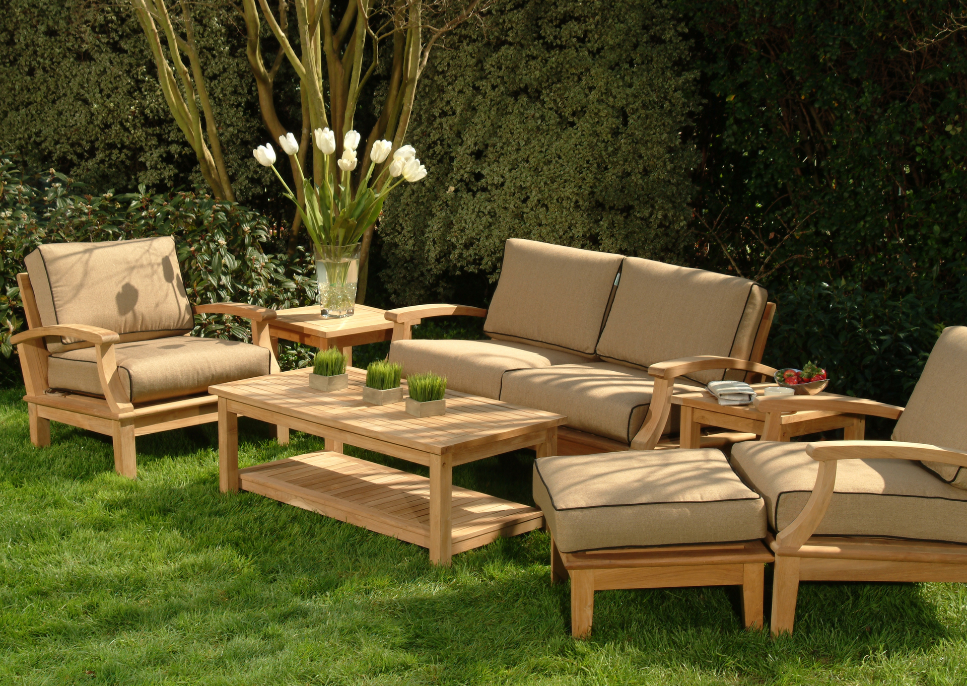 Outdoor living room set with beige cushions, on green grass, tulips in vase.