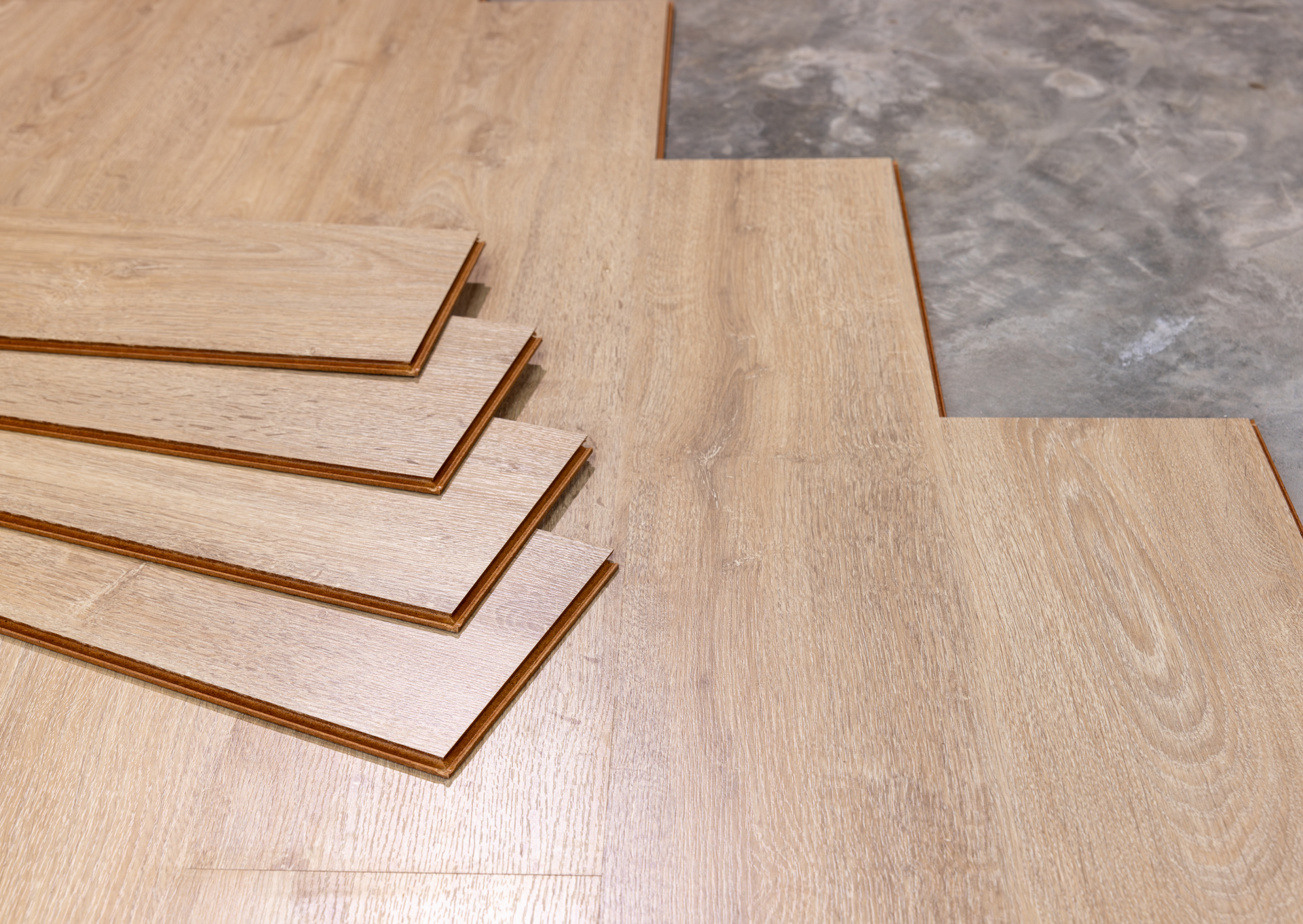 Light wood laminate flooring being installed on a concrete surface.