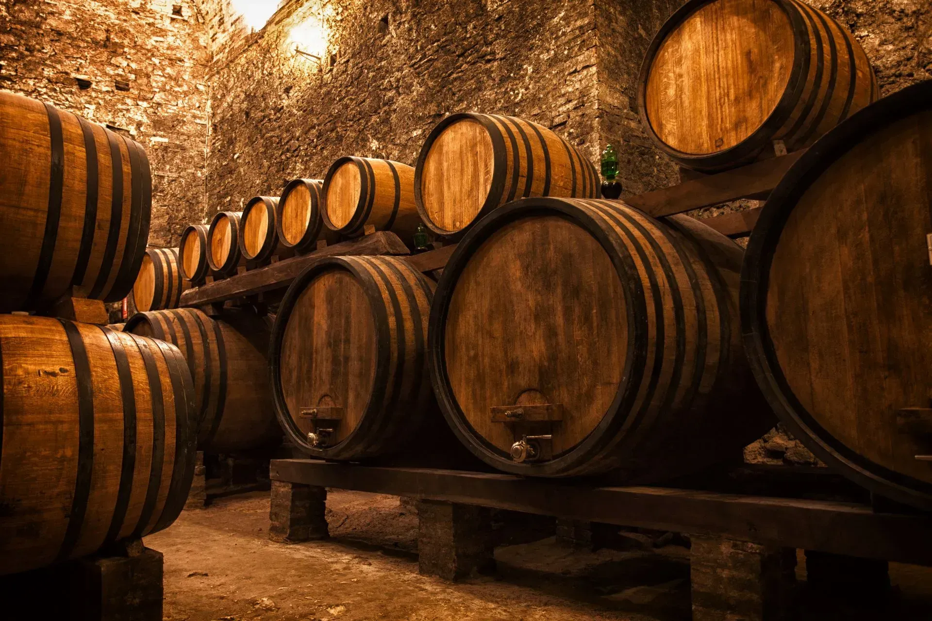 Wooden barrels in a dimly lit wine cellar, stacked on racks.
