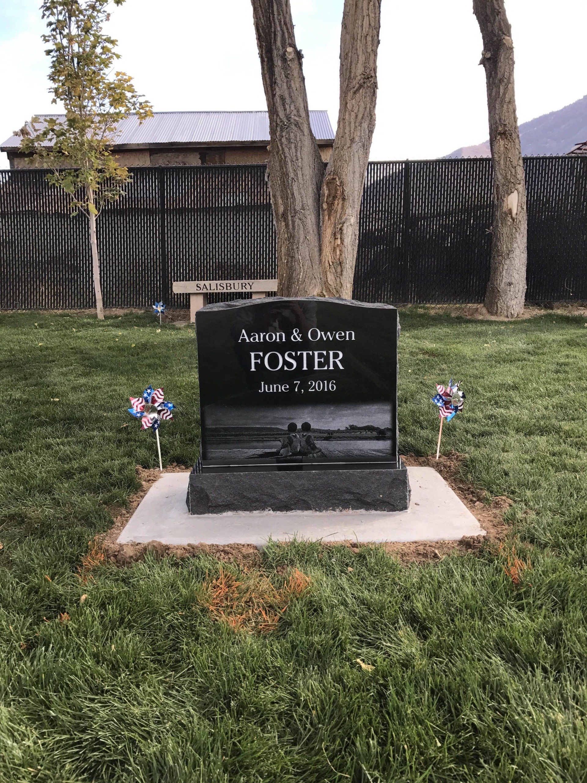 Black headstone for Foster, with an image of a person and a lake. Two pinwheels on either side.