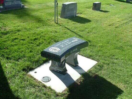 A black granite bench in a grassy cemetery, with engraved lettering.