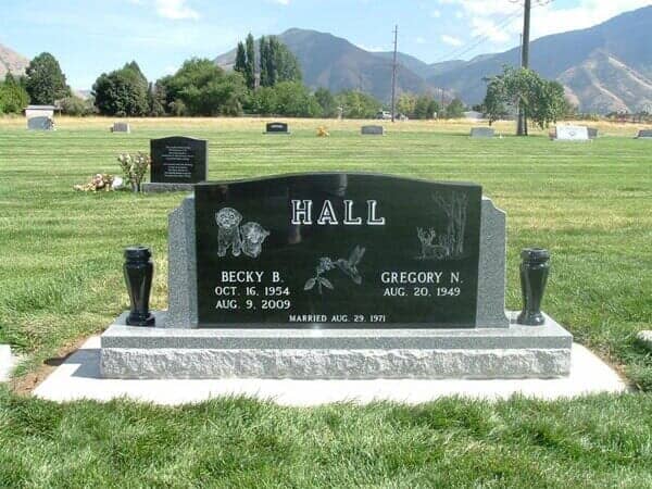 Headstone in a grassy cemetery with the name HALL. Dates and two urns on a sunny day.