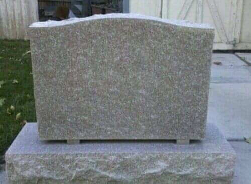 Gray granite headstone on a rectangular base, outdoors.