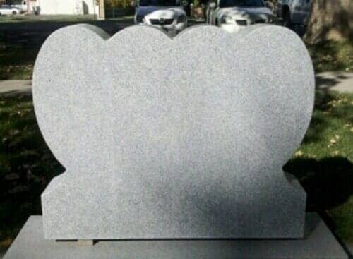 Gray heart-shaped granite headstone in a cemetery with cars in the background.