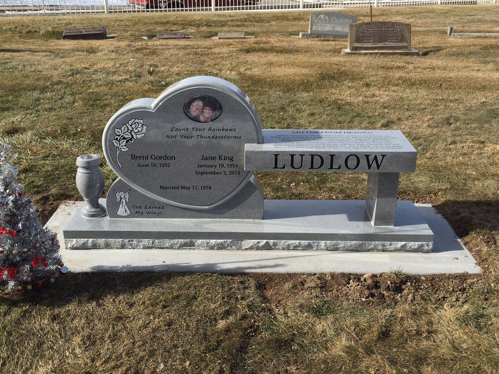 Heart-shaped gravestone with a bench. The Ludlow family name is on the bench. Includes an image of people.