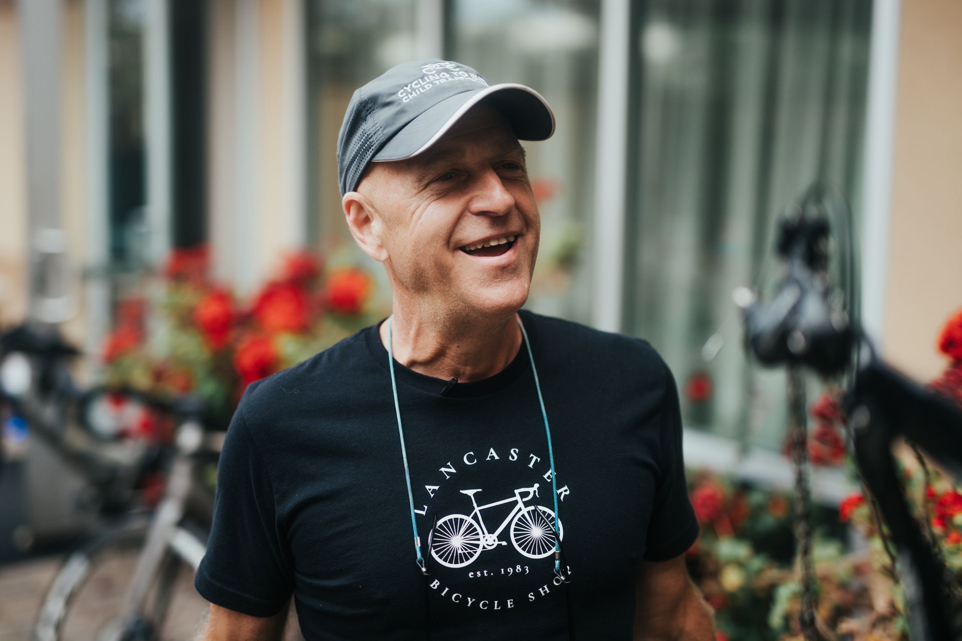 A man wearing a hat and a t-shirt with a bicycle on it is smiling.
