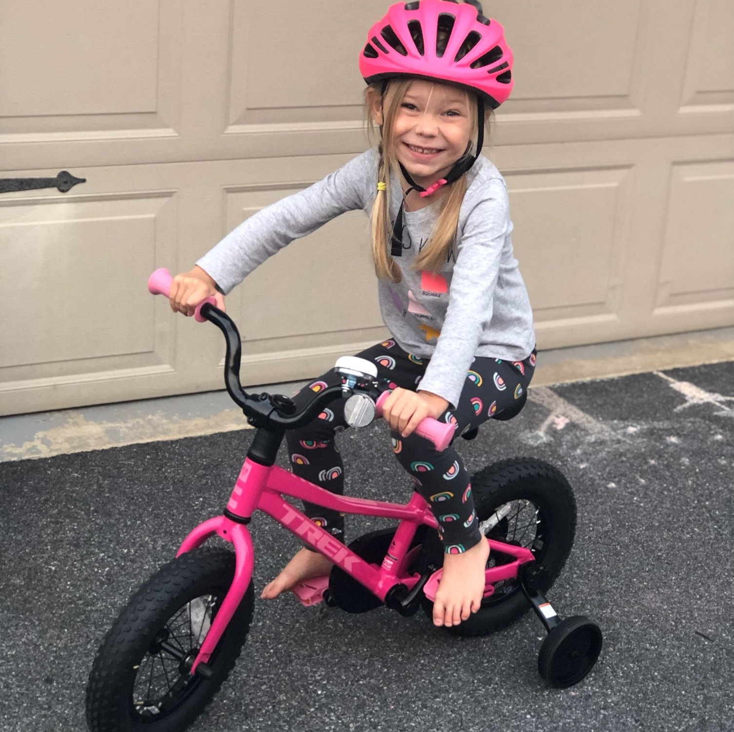 A little girl wearing a pink helmet is riding a pink trek bike