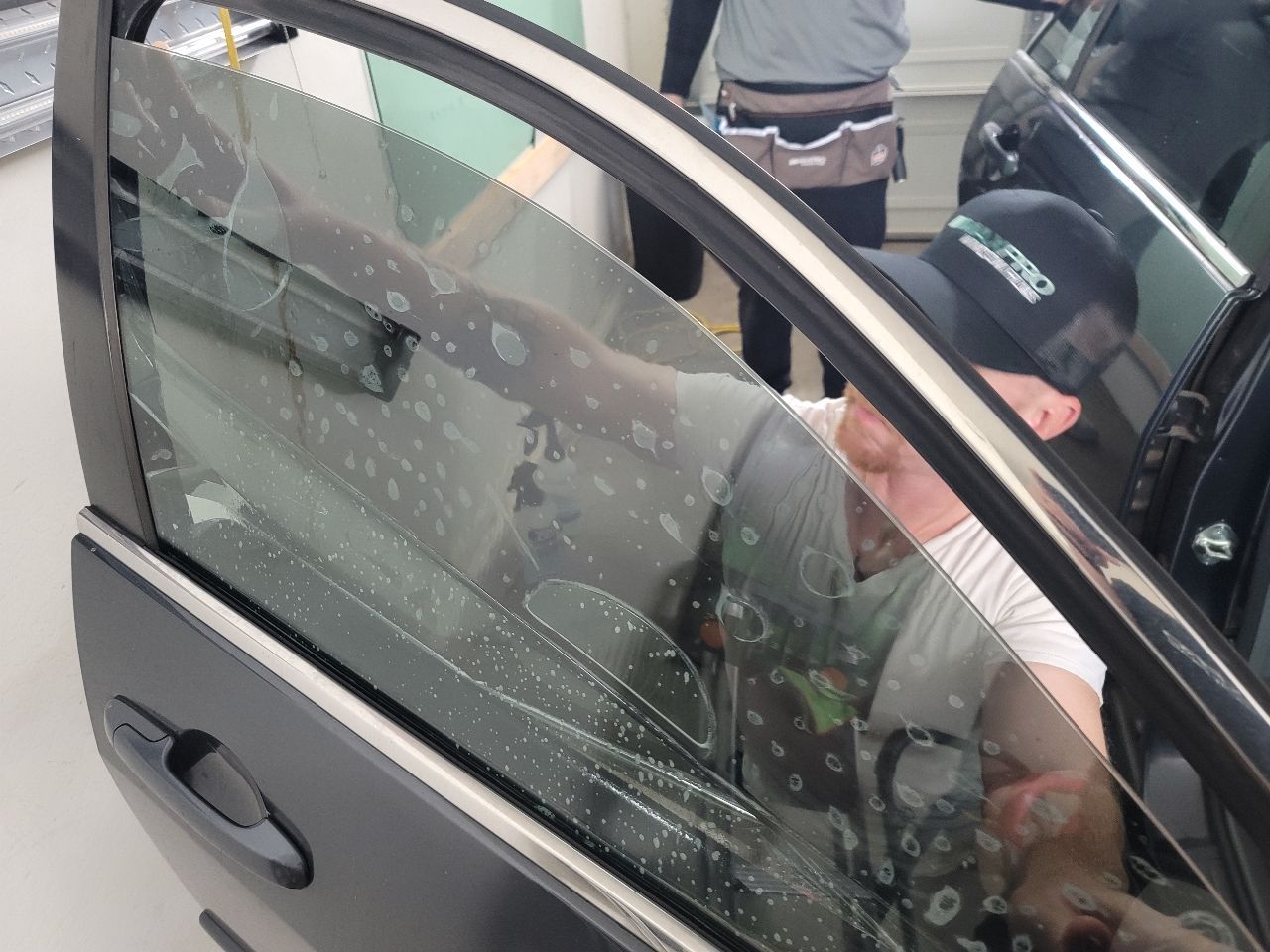 A window tint installer putting window film on a door glass before pushing the bubbles out of the window film.
