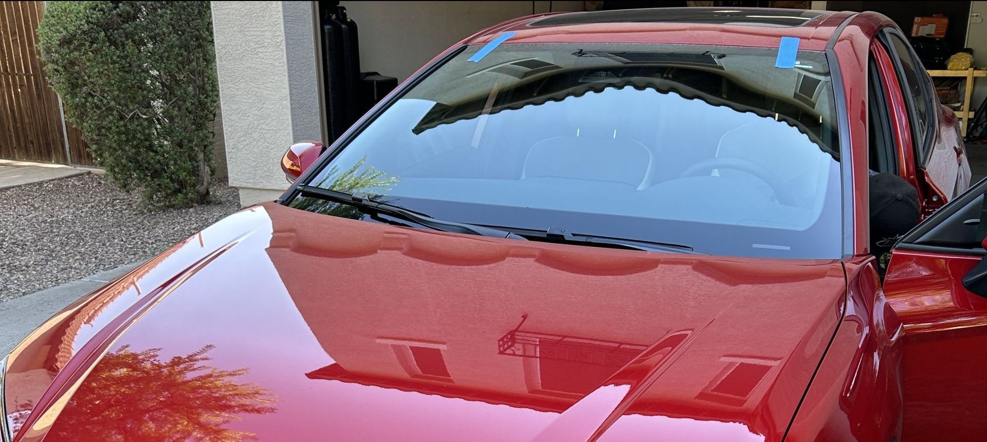 Red car with a new windshield installed and blue tape on the top of the windshield.