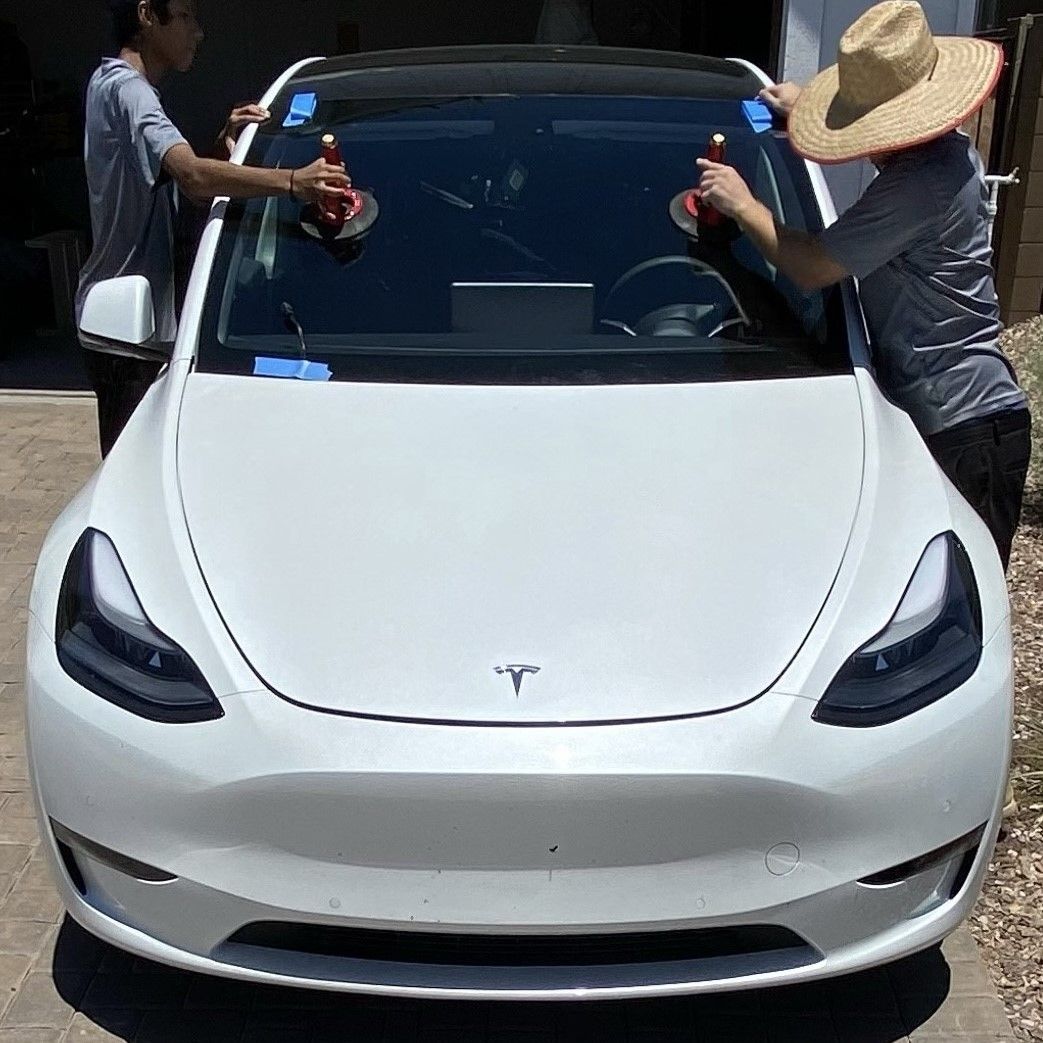 Auto Glass technicians doing a windshield replacement on a Tesla in the driveway.