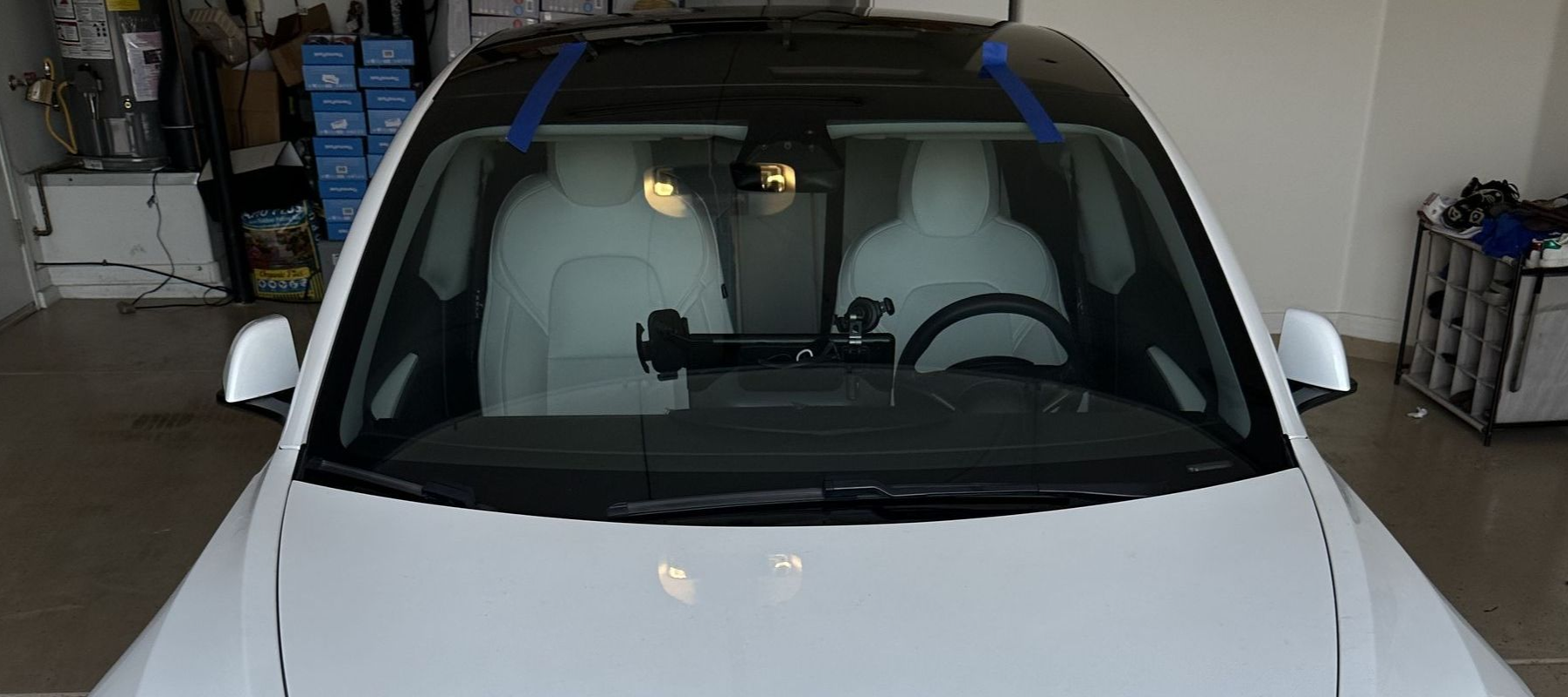 Tesla windshield installed with blue tape holding the glass to the vehicle.