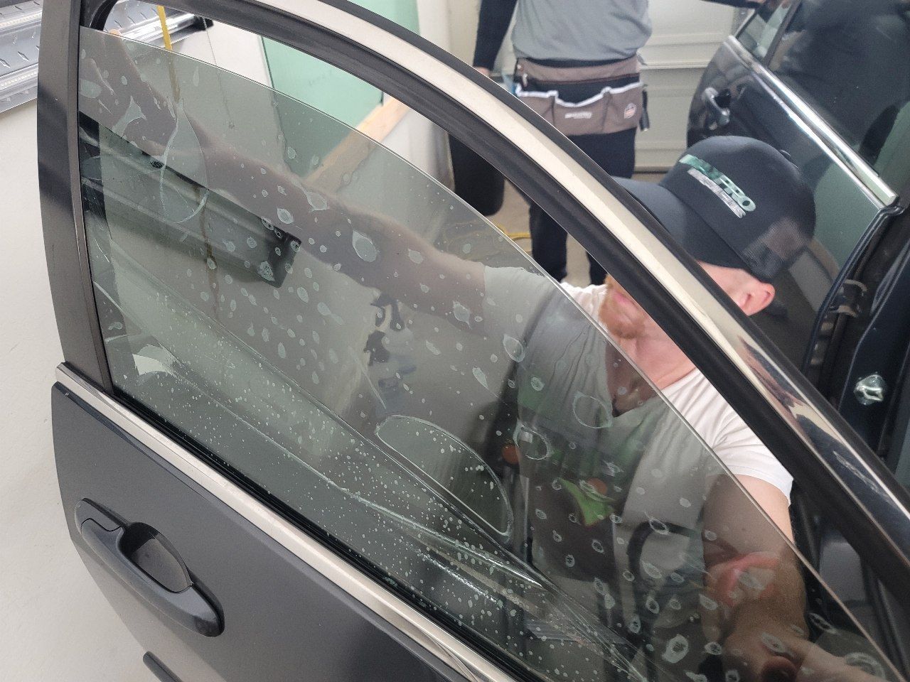 A window tint installer putting window film on a door glass before pushing the bubbles out of the window film.