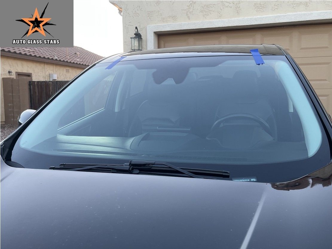 Windshield installed with blue tape hold it in place on a vehicle in the driveway.