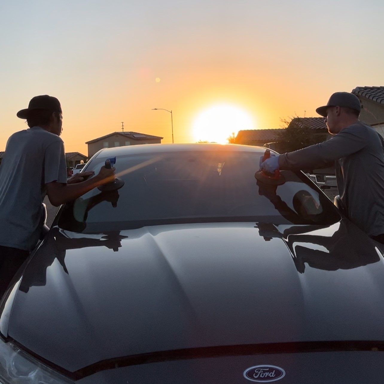 Early morning auto glass technicians replacing a windshield on a Ford car with the sunrise in the background.