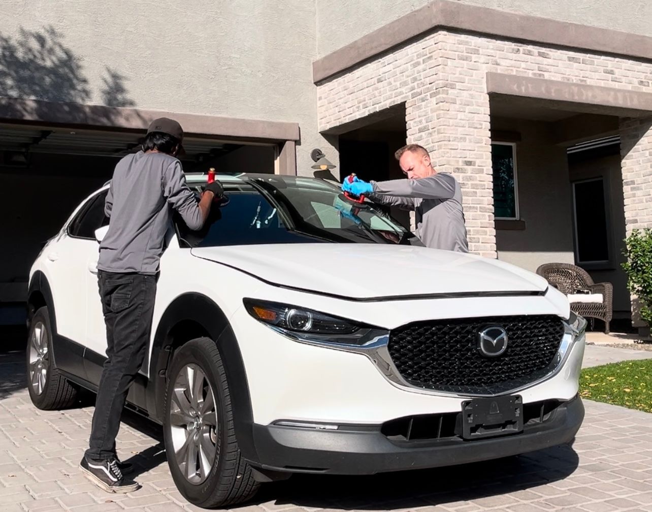 Windshield being replaced on a white Mazda in the driveway.
