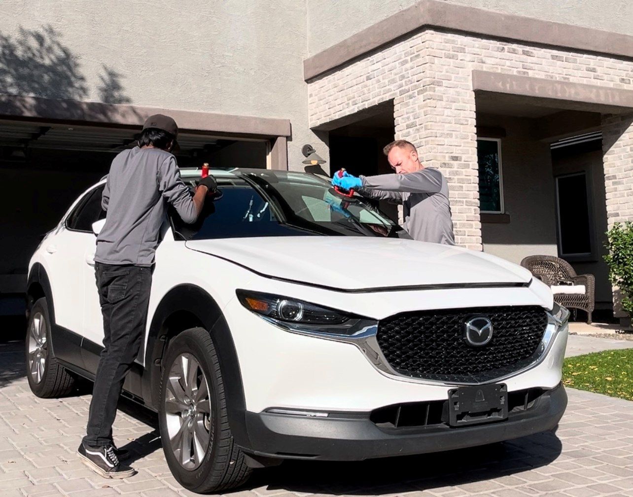Windshield replacement with two auto glass technicians on a white Mazda.