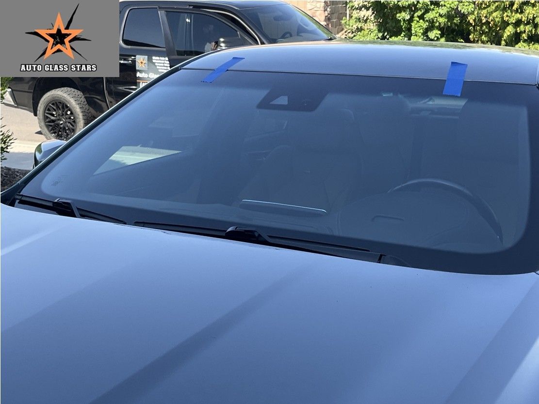 Mobile windshield replacement on a vehicle with the auto glass technician's truck in the background.