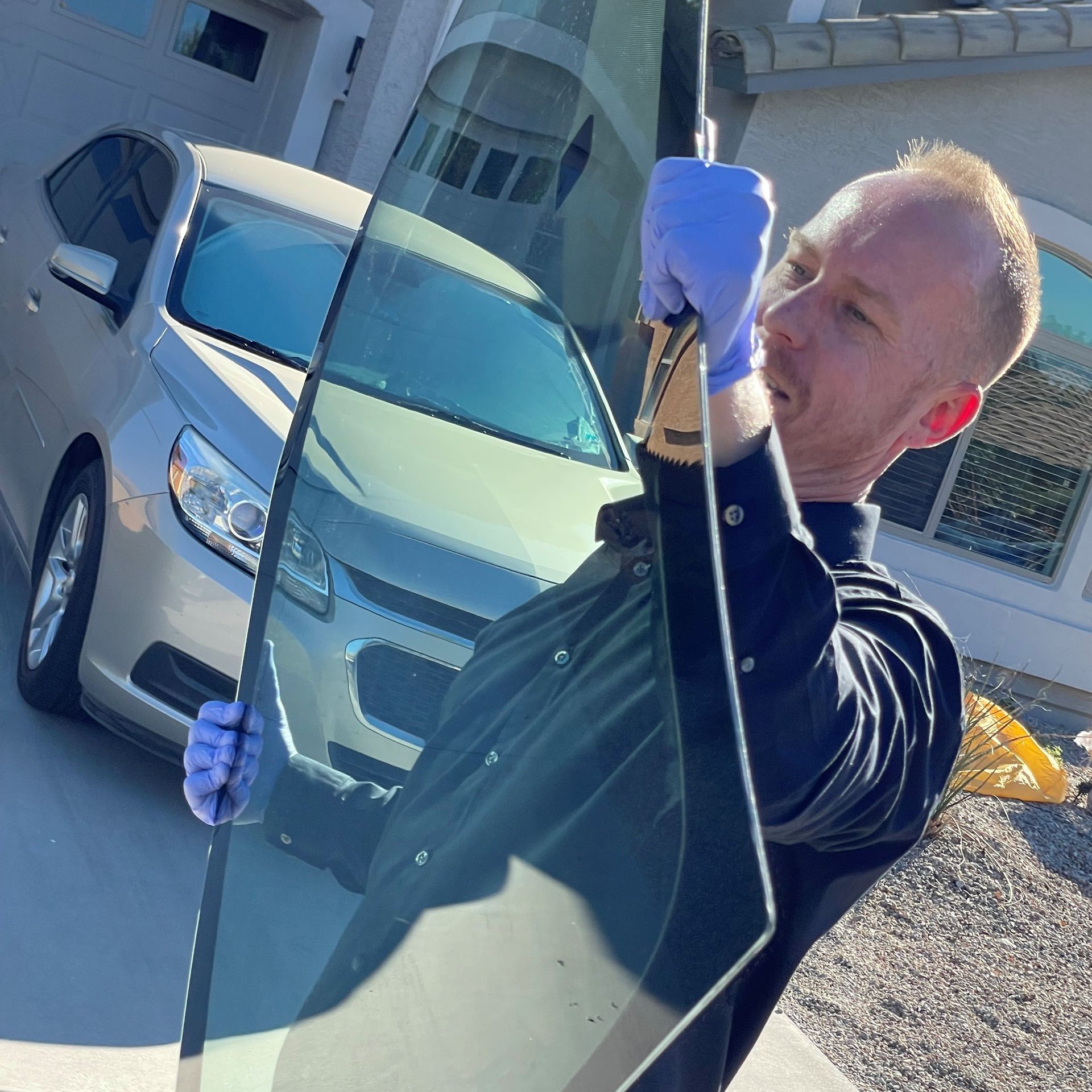 Auto glass technician replacing a windshield in front of a car.