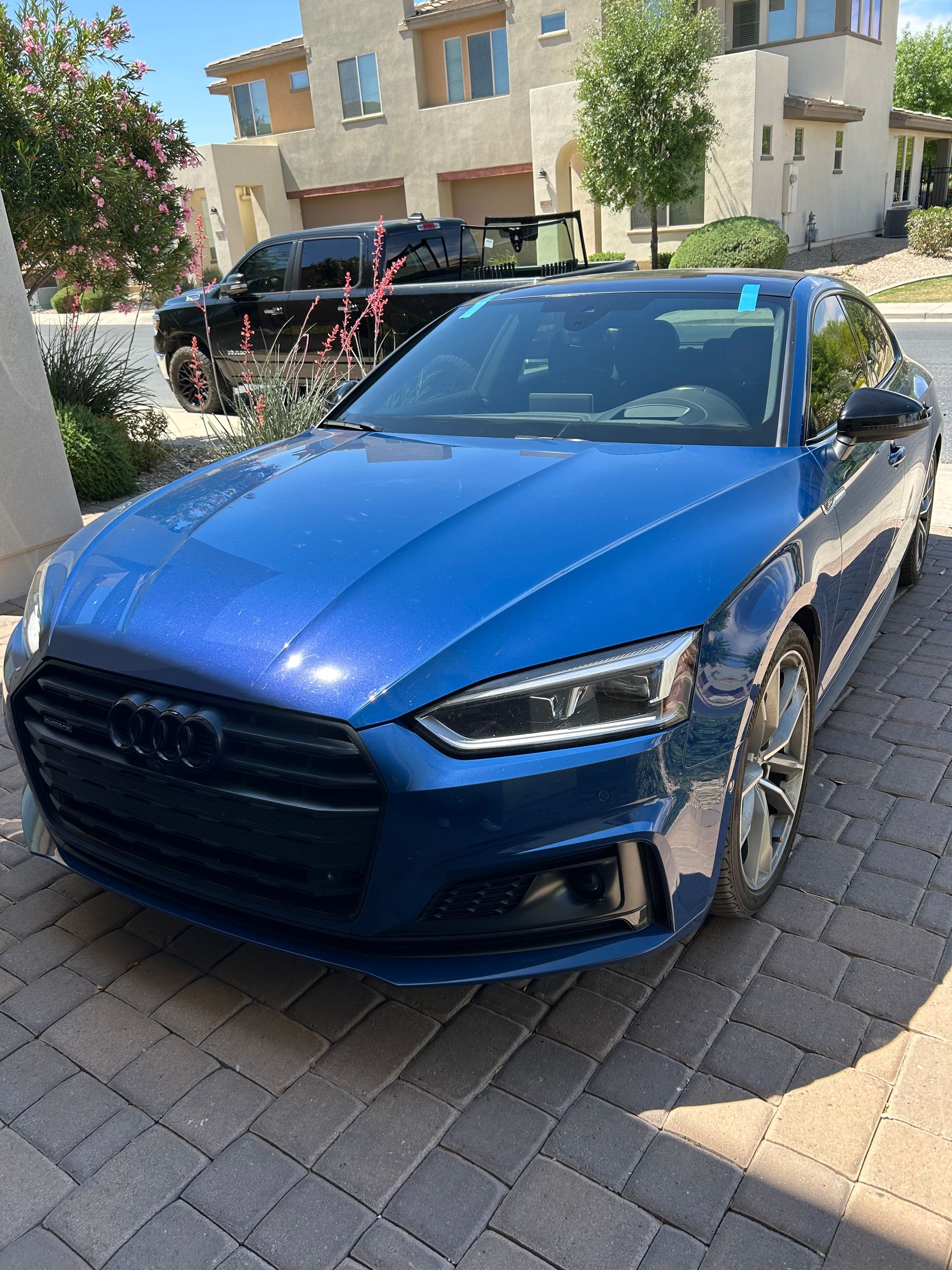 Blue Audi with a windshield replaced and the mobile auto glass technician's truck in the background with windshields.