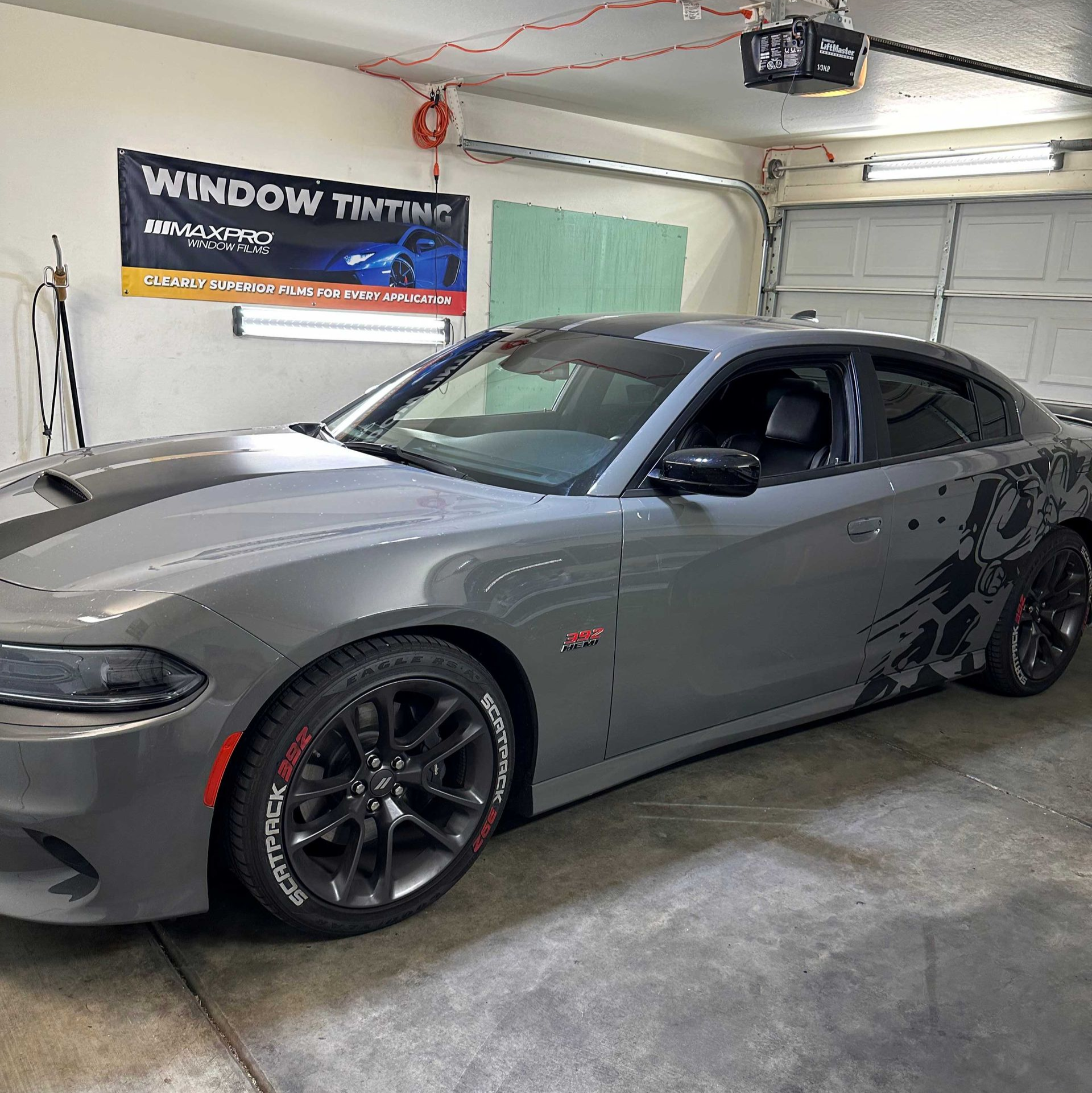 A Dodge Charge in a window tinting shop with a dark tint on the windshield visor strip.