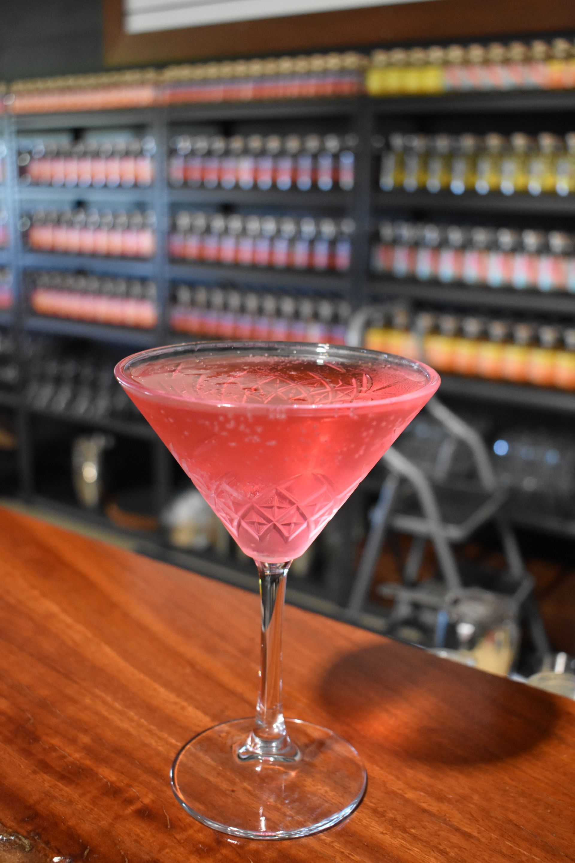 A pink martini is sitting on a wooden bar.