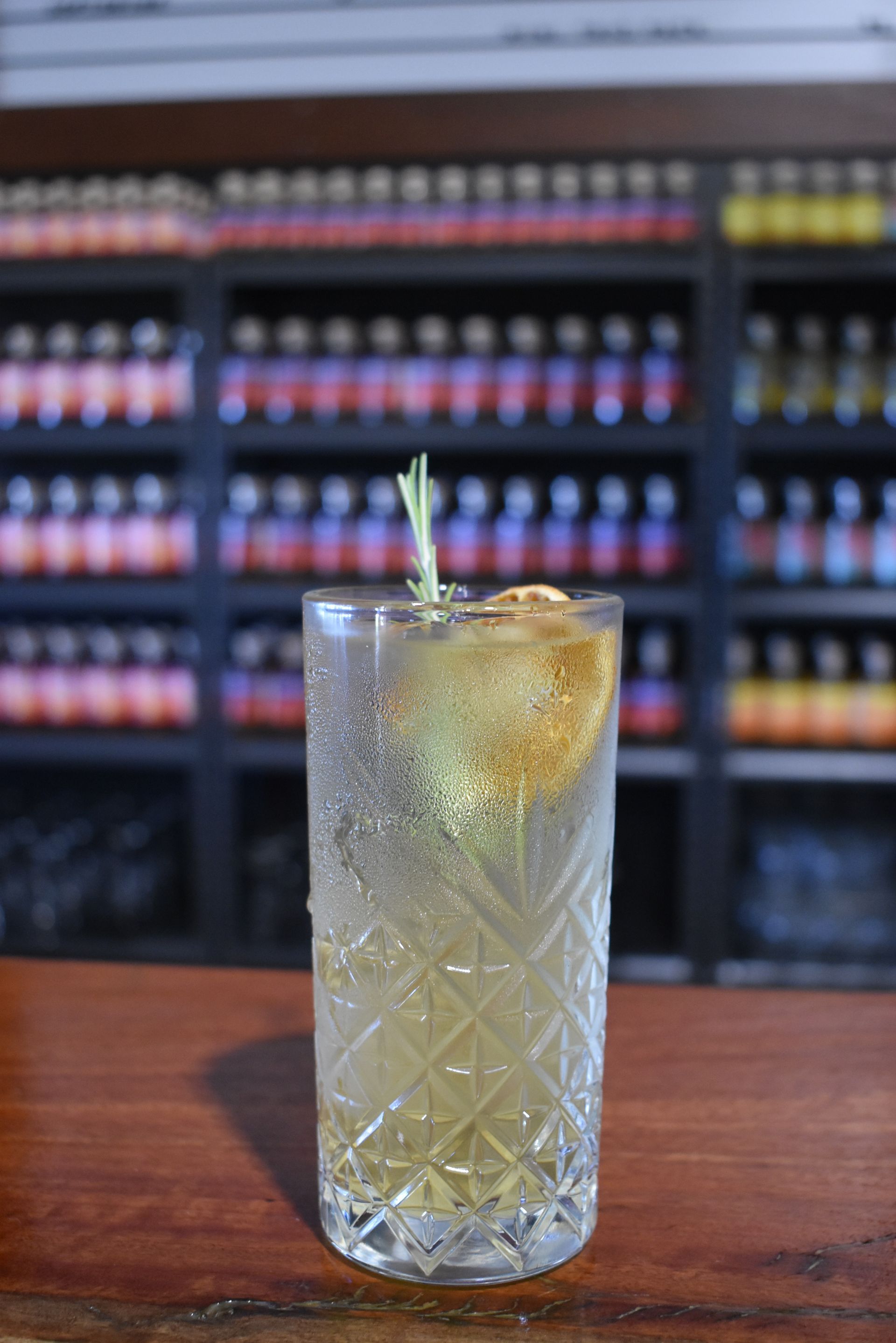 A tall glass filled with a drink and a slice of lemon on a bar.