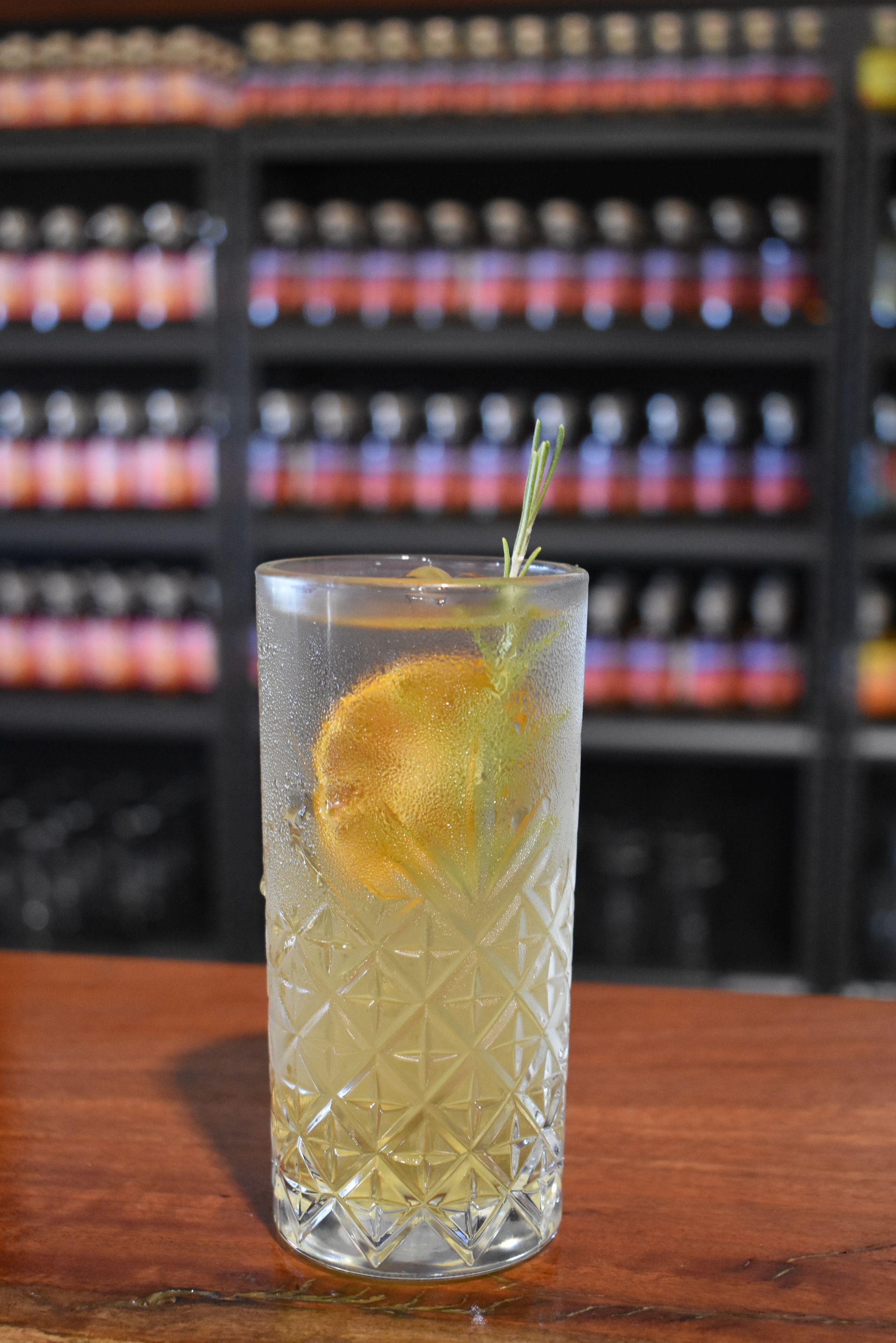 A tall glass filled with a drink and a lemon slice on a bar.