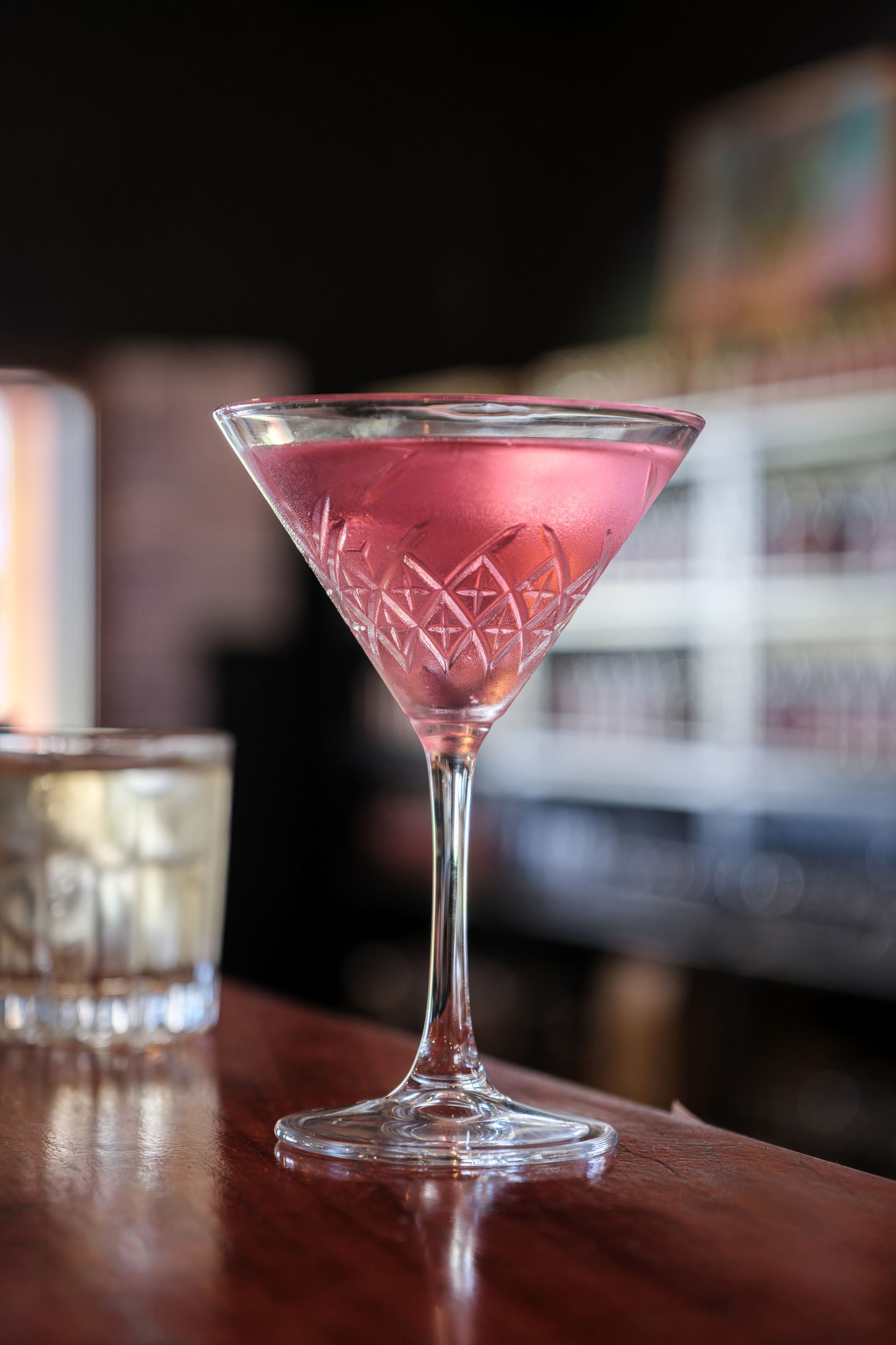 a martini glass filled with a pink liquid is sitting on a bar .