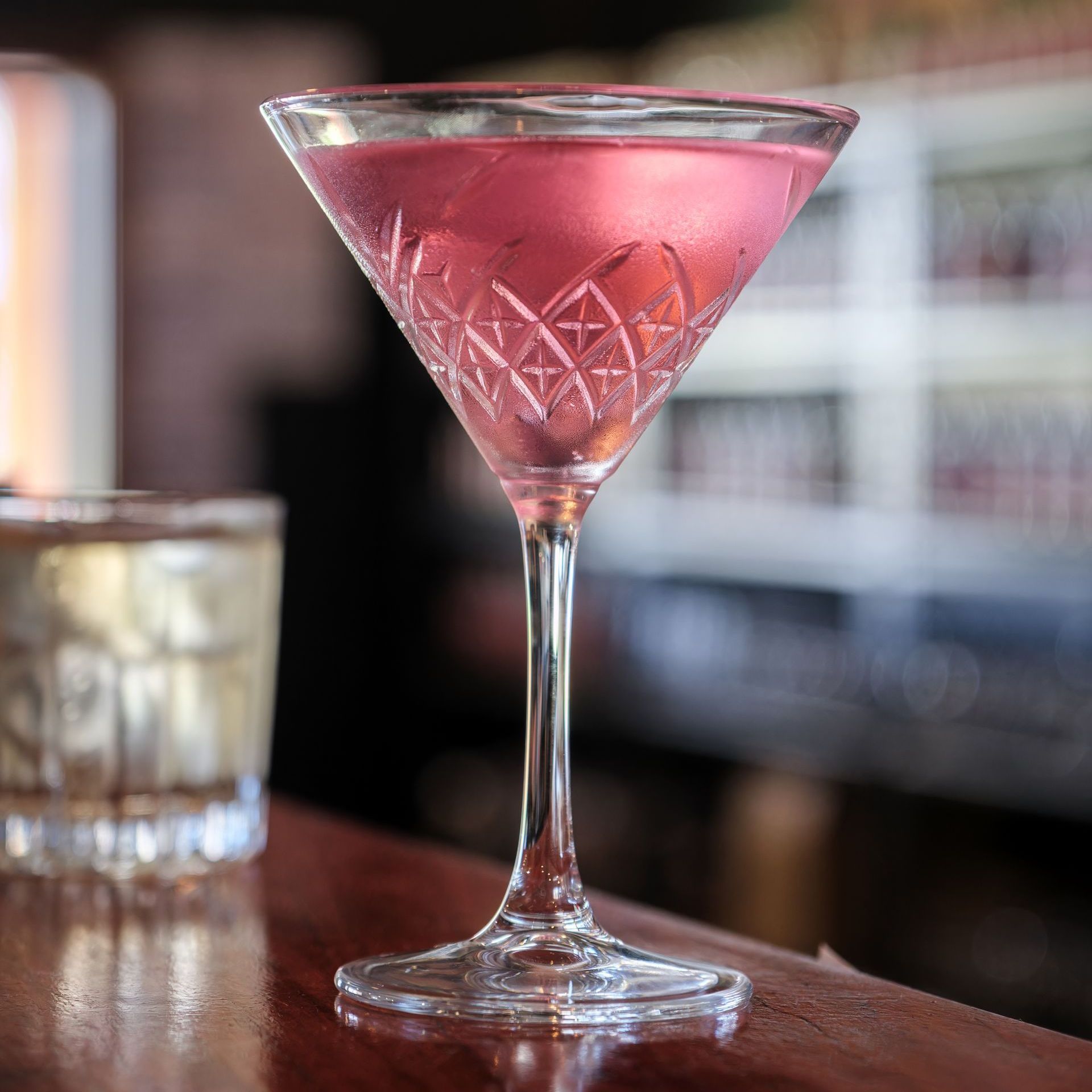 A pink cocktail in a martini glass on a bar.