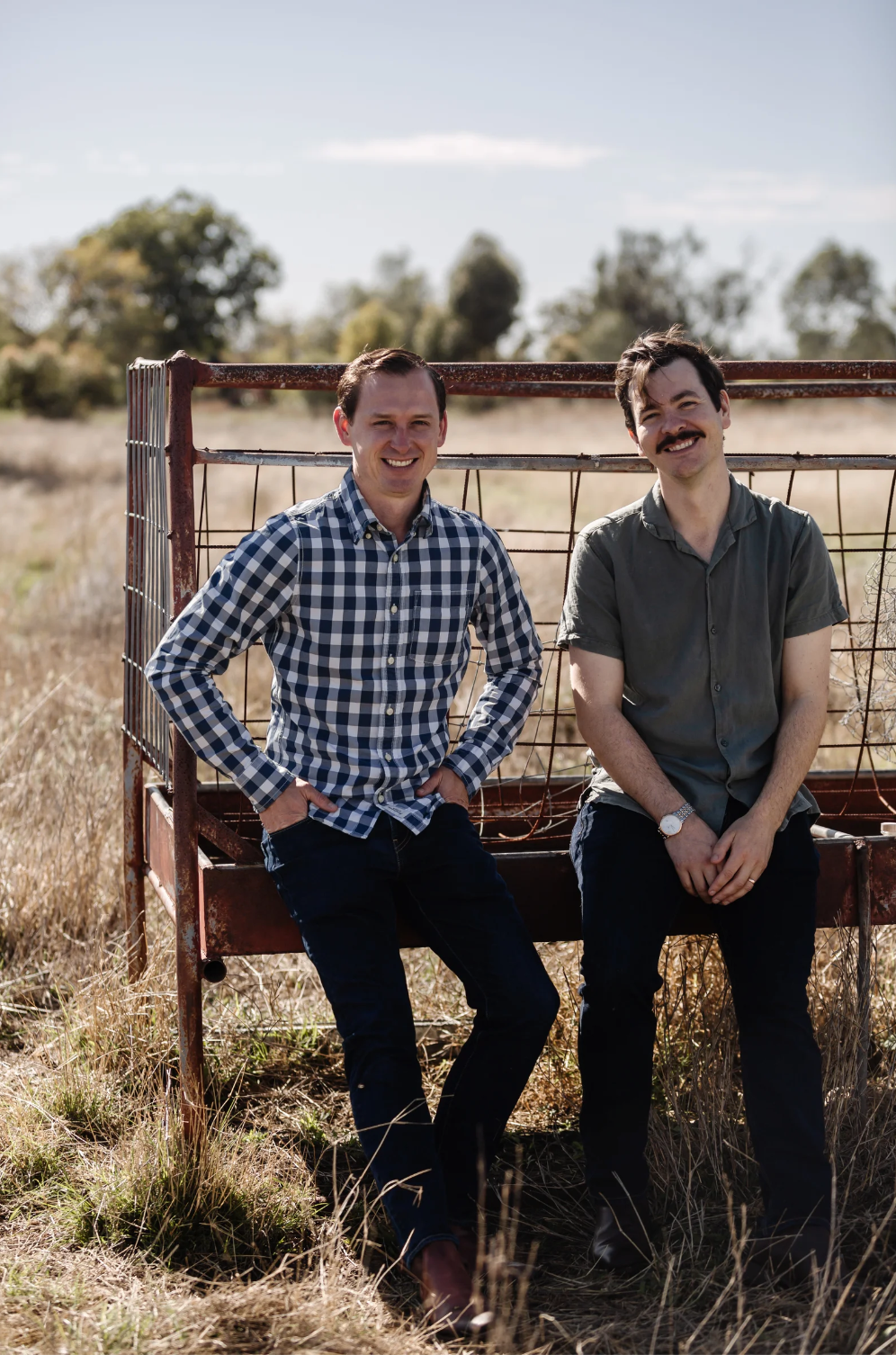 Two men are sitting on a bench in a field.