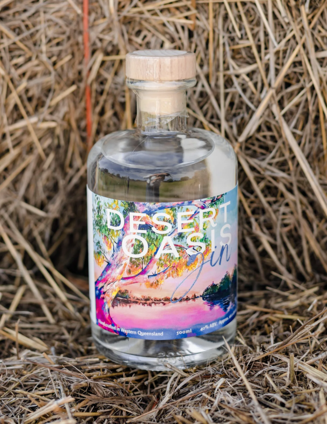 a bottle of desert oasis gin is sitting on top of a pile of hay .
