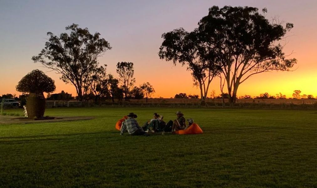 A group of people are sitting in a field at sunset.