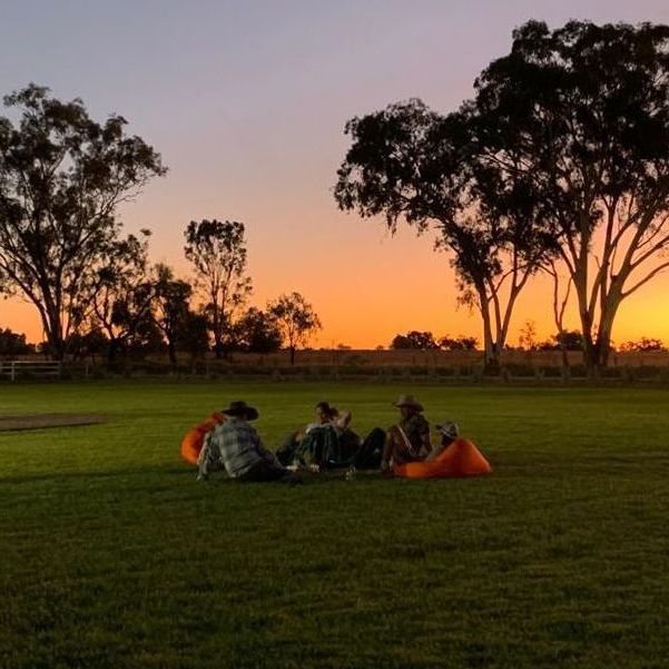 A group of people sitting in a field at sunset